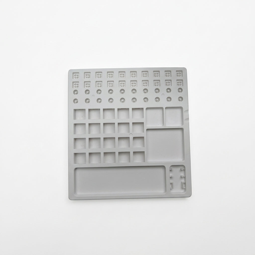 Top-down view of white plastic switch lube station tray featuring stem holders, spring slots, and parts compartments.