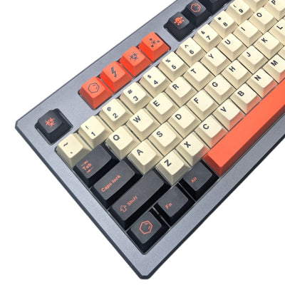 A close-up of a mechanical keyboard showing the keycap layout. The keys feature a mix of cream, burnt orange, and matte black, set against a dark gray keyboard frame.