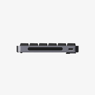 A close-up side view of a compact mechanical keyboard showing the side profile, keycaps, a horizontal slot, and a USB-C port, set against a solid white background.