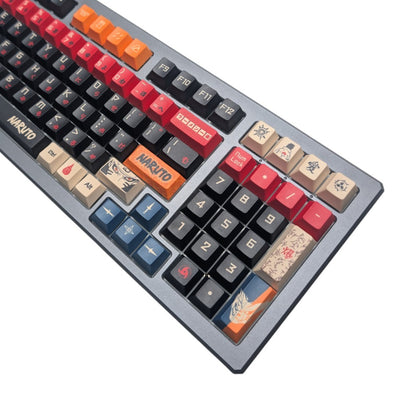 A close-up of a mechanical keyboard with custom anime-themed keycaps. The keys feature various colors and designs, including orange, red, blue, beige, and black, with some keys printed with the Naruto logo or character art.