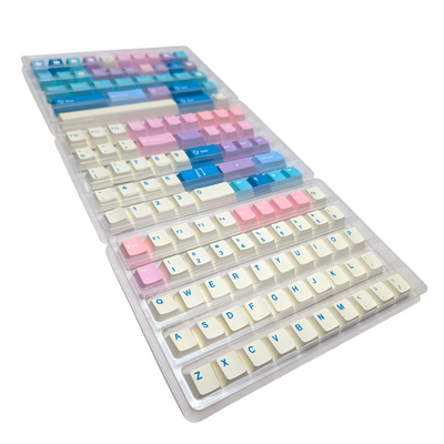 Three trays displaying pastel pink, blue, and cream PBT keycaps in various sizes and layouts.