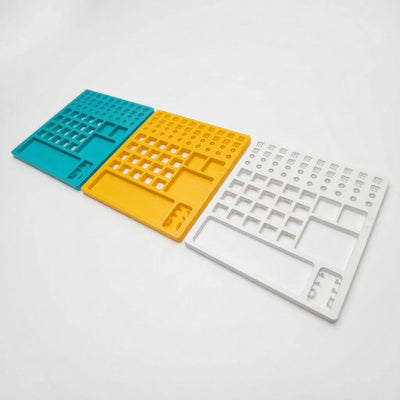 Lineup of all three color options for the plastic switch lube station in teal, yellow, and white.