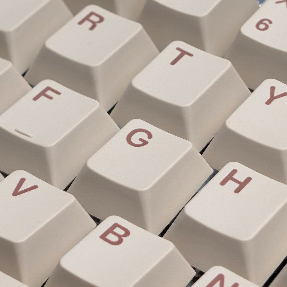 Close-up of cream-colored mechanical keyboard keycaps with muted red lettering, showing keys such as R, T, F, G, B, and H.