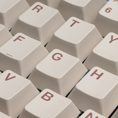 Close-up of cream-colored mechanical keyboard keycaps with muted red lettering, showing keys such as R, T, F, G, B, and H.